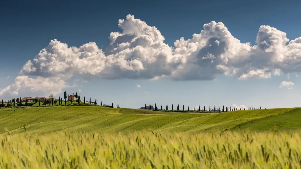 Paesaggio collinare toscano con cipressi e casale sotto un cielo estivo